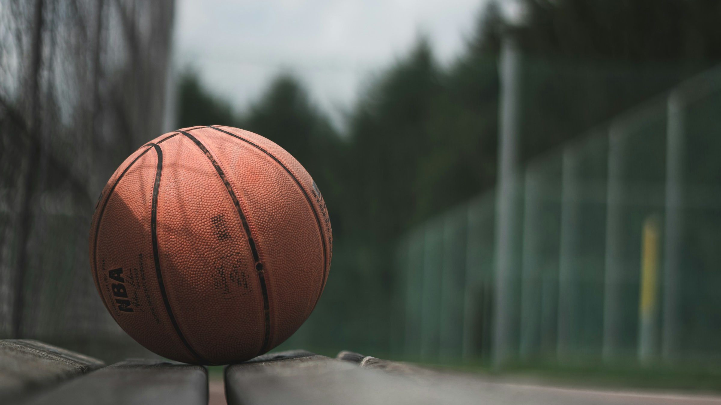A basketball sitting on a bench. The mood is gloomy near this basketball court with no people around. The sky is overcast.